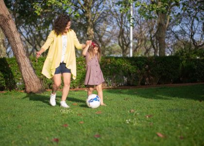 A mother and daughter enjoying a sunny day playing soccer in a lush green park.